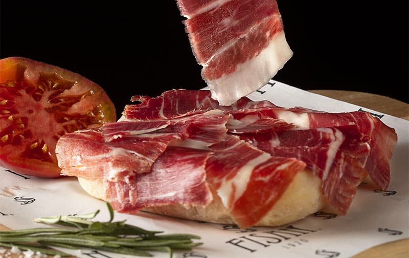 Jamón de bellota ibérico cortado a mano por maestros cortadores, indispensable para preparar el bocadillo de jamón ibérico perfecto.